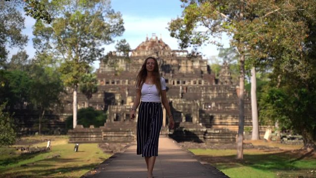 A young woman walks down a path in front of Hindu Temple Baphuon, Angkor Cambodia, slow motion