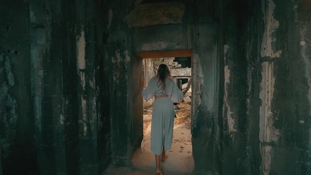 Following a young woman as she walks out of a stone doorway, Ta Prohm Temple, Cambodia, slow motion