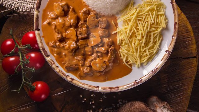 Meat stroganoff with rice and french fries on dish. Top view with smoke.