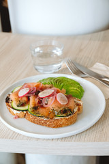 Salmon toast with avocado and vegs in the modern cafe. Fancy cafe and modern healthy snack concept. Take away, delivery menu item