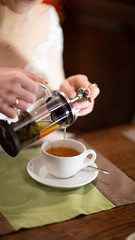 Pours herbal tea into a mug.