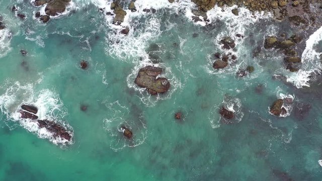 Top down view of the ocean flowing and cascading over a jagged shoreline