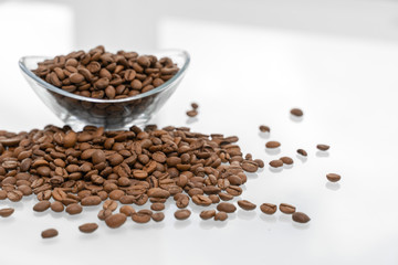 scattering of coffee beans on a glossy bright table with reflection. a bowl with grains in the background. breakfast concept
