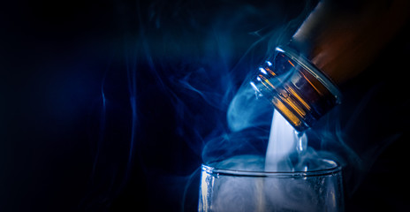 Macro shoot a bottle of liquor from which there is smoke or steam while the drink is being poured into the glass. Bad sinful habits of the nightlife in the city.