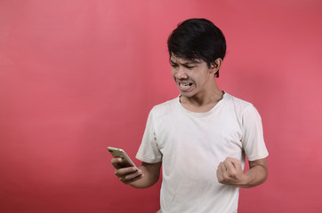 The face of Asian man is shocked what he sees in the smartphone. Asian men wearing white t shirts isolated on a red background