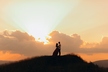 The silhouette of a young couple in love at sunset, they embrace kiss and look at each other with tenderness. Slow motion. Young couple at sunset.