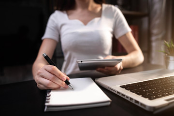 Female businessman use a laptop computer and take notes in the notebook at the office desk