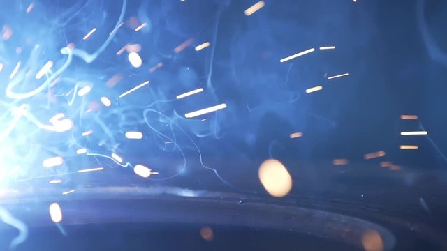 Flight of sparks generated by modern Industrial Robot welding machine active on industrial plant. Automation welding mechanical procedure. Metal iron laser argon welding robot in factory. Slow motion