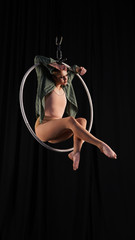 Graceful girl aerialist hangs on hands in a white ring on a black background, the girl has a mysterious look, a professional circus artist dances in an aerial hoop © Artem