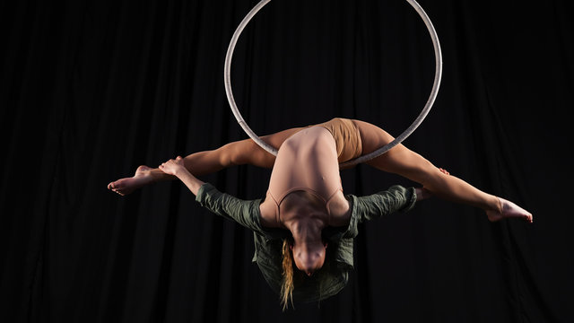 Professional circus aerialist performs splits on the ring. young, athletic, flexible gymnast on a black background performs tricks in the air hoop. Acrobat back bend