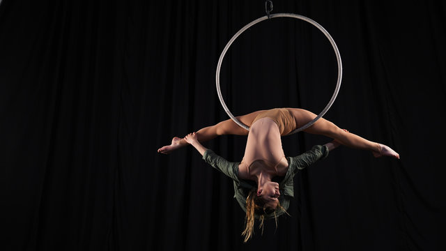 Girl female gymnast performs gymnastic pose for flexibility. Beautiful split in a woman. Professional circus actress in aerial hoop on a black background