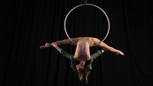 Girl female gymnast performs gymnastic pose for flexibility. Beautiful split in a woman. Professional circus actress in aerial hoop on a black background