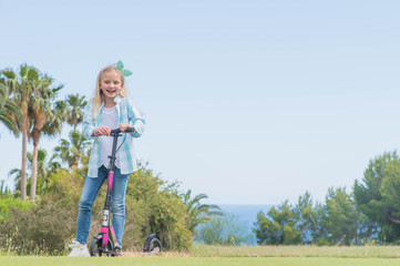 Active little girl with scooter  in park outdoors on summer day.  Summer time fun