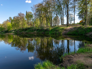 Fototapeta na wymiar spring landscape with a river, in the waters of which clouds are reflected, the banks of the river are covered with trees, the first spring greenery in nature, stones and green grass in the foreground