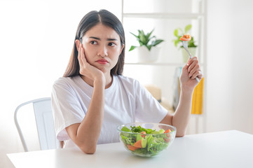 The unhappy dieting Asian girl has a boring expression when she eats vegetables. She have sad face. diet, clean food, Healthy food and vegan concept.