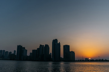 Fototapeta na wymiar Evening sunset on the seashore and city silhouettes of tall houses on the other Bank | UNITED ARAB EMIRATES, SHARJAH - 17 OCTOBER 2017.