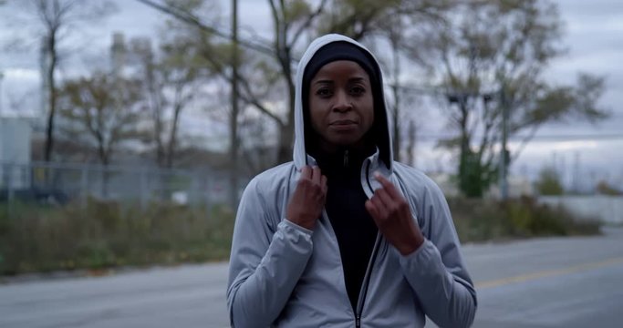 Jogger wearing running jacket putting on hood then zipping up jacket looking determined, preparing to go for a run