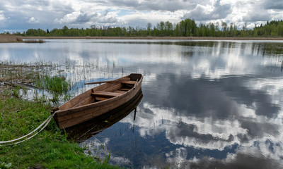 landscape with calm lake water, wonderful cloud reflections in the lake water, a beautiful brown wooden boat on the lake shore