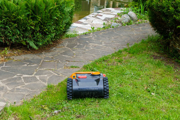 Robotic lawnmower at work. A pond and a flower bed are visible on the horizon