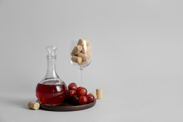 Decanter of wine with glass and corks on grey background