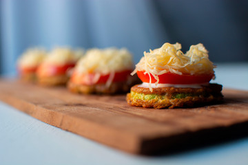 appetizer in a row on a wooden board. i zucchini with sauce, tomatoes and cheese.