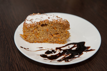 Tasty carrot cake with powdered sugar and chocolate syrup on white plate