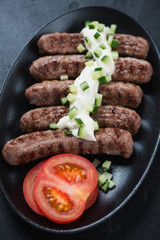 Close-up of grilled serbian cevapi or cevapcici sausages topped with kajmak cheese on a black plate, selective focus, vertical shot