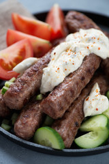 Close-up of bbq serbian cevapi sausages with kajmak cheese and fresh vegetables, vertical shot, selective focus
