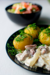 mushrooms with onions and sauce and potatoes on a black plate.