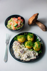 Young potato with mushrooms and lettuce on black dishes. raw mushroom on the table with food.