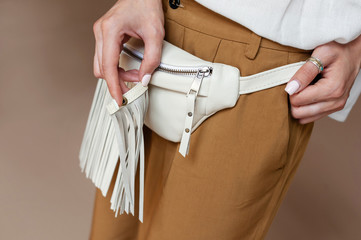 Girl in brown trousers with a white bag on the waist. The model shows a separate fringe. Designer...