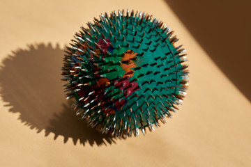 A green-coloured massage ball with rubber and metal needles on an orange surface. Advertising, thematic and subject shooting. For relaxation and health.