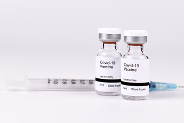Small vial bottles with text 'Covid-19 vaccine' with syringe in blurry background, a concept for...