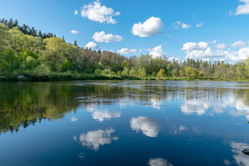 Fototapeta na wymiar spring landscape with a river, in the waters of which clouds are reflected, the river banks are covered with trees, the first spring greenery in nature