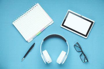 White wireless headphones, tablet, notepad on the blue background.