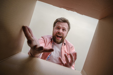 Upset man found the wrong order in the unpacked delivered box and inquiringly makes a gesture with hands. Unboxing inside view.