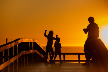 Fototapeta na wymiar Sunset on the beach with silhouette of father with children, back