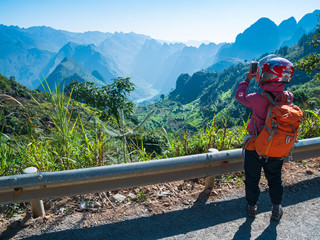 Fototapeta na wymiar biker with helmet taking picture at Ha Giang karst geopark mountain landscape in North Vietnam. Unique canyon with blue river. Ha Giang motorbike loop, famous travel destination bikers easy riders.