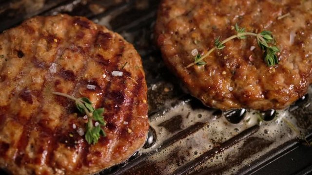 Grilled hamburgers on the grill. Burger cutlet is cooked in a grill pan, thyme, steam, smoke, fire. Butter is melted. Grill food. Slow motion.