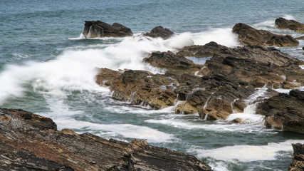 Fototapeta na wymiar Brandungswelle läuft über Felsen vor der Küste und lässt Wasser herabströmen