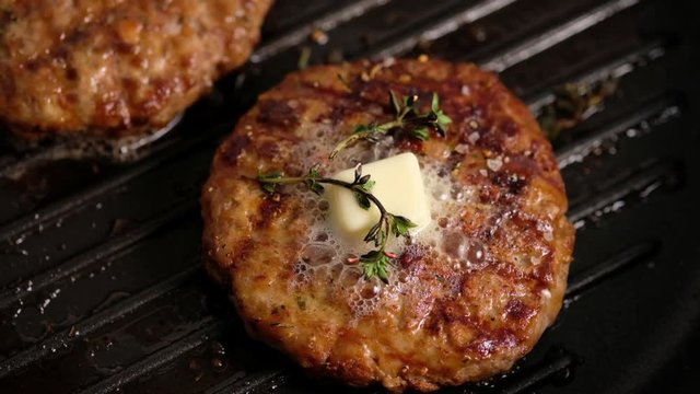 Grilled hamburgers on the grill. Burger cutlet is cooked in a grill pan, thyme, steam, smoke, fire. Butter is melted. Grill food. Slow motion.
