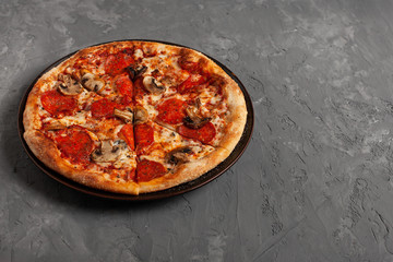 Tasty pizza with salame and mushrooms. Pizza on grey concrete background with copy space. Top view of sliced pizza. 