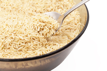 A glass plate contains brown rice with a spoon on a white background. Close-up with space for the inscription.