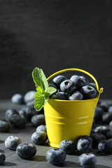 ripe blueberries in a small bucket on a gray background