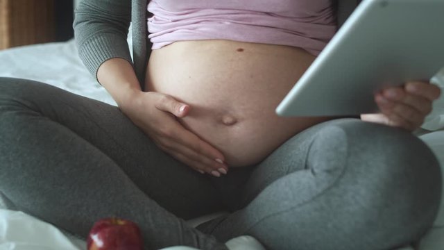 Tracking left video of unrecognizable pregnant woman using tablet in bed. Shot with RED helium camera in 8K 