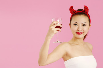 Obraz na płótnie Canvas Woman with devil's horns holding a glass of red wine