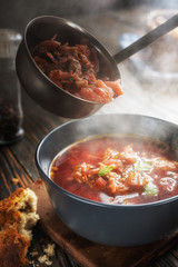 Tomato soup with vegetables and meat is poured into a bowl from the ladle from which steam comes, tasty, appetizing traditional Ukrainian borsch, close-up, shallow depth of field, selective focus