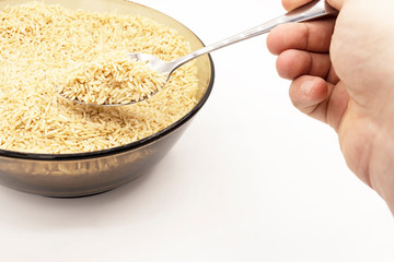 Glass plate with brown long-grain rice. Above the plate is a hand holding a spoon with rice.