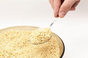 Part of a glass plate with brown long-grain rice on a white background. A spoon of rice is in my hand.