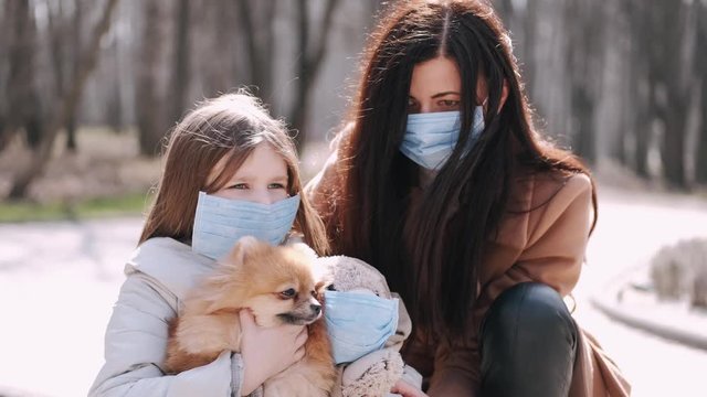 European mother and her daughter are walking with a dog. It's quarantine period so the mother and her child are wearing disposable masks to protect themselves from virus. The parent and chils are